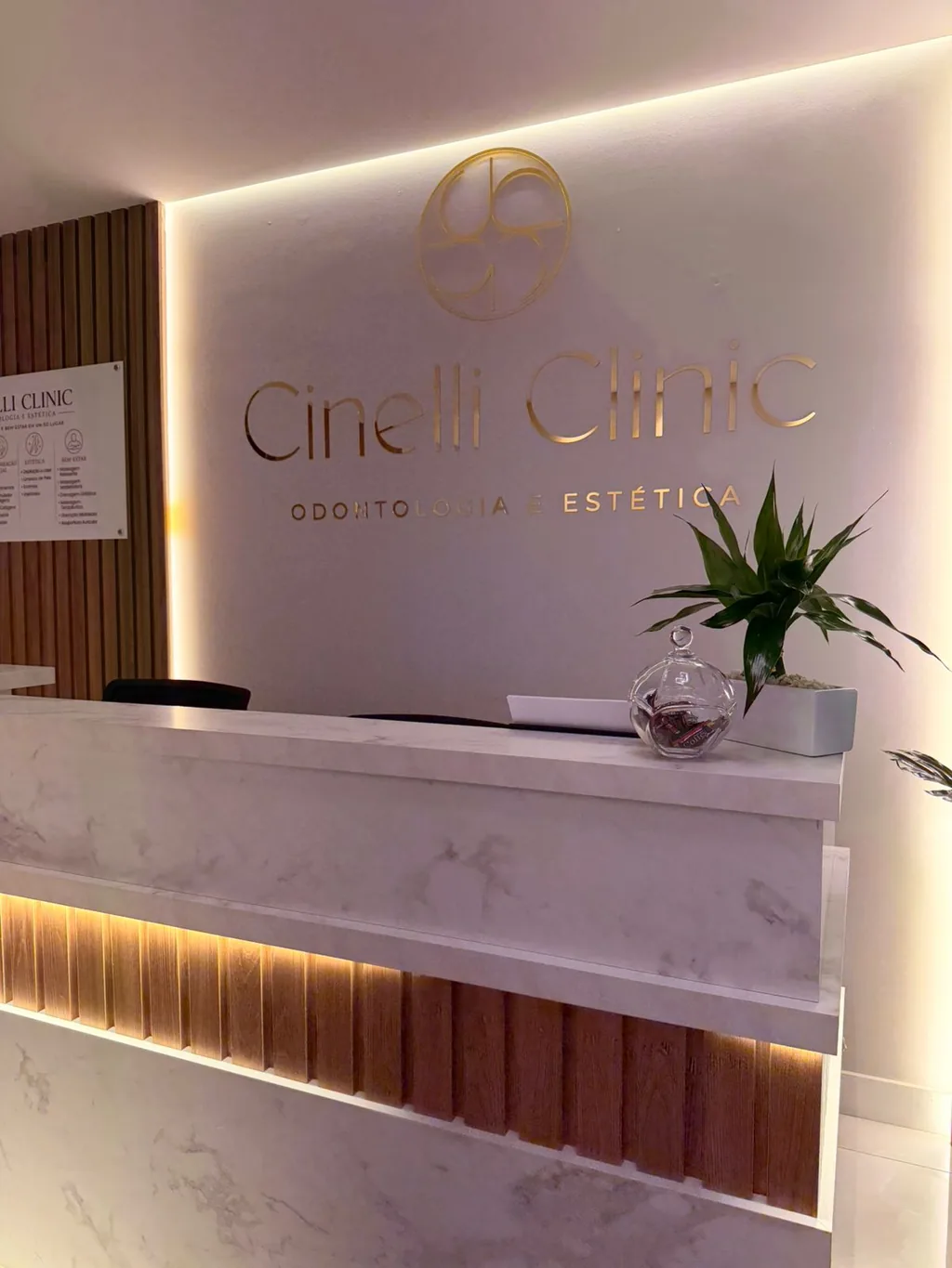 Recepção da Cinelli Clinic, com o logotipo iluminado sobre o balcão de mármore